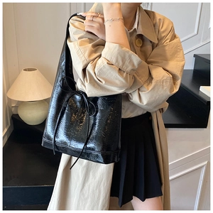 Detail of black glossy leather shoulder bag with decorative bow and textured finish