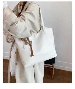 Close-up of a large white leather tote bag with a brown T-charm worn by a model in a trench coat