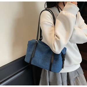 Vista laterale della borsa tote in denim blu con manici in pelle nera indossata