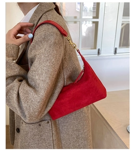 Detail of red suede crescent bag with gold hardware worn on a brown tweed coat