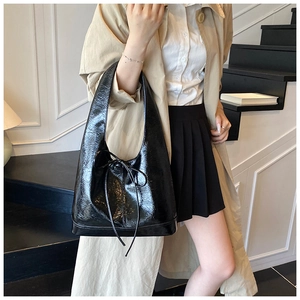 Fashionable black glossy tote bag with delicate bow detail carried by a model
