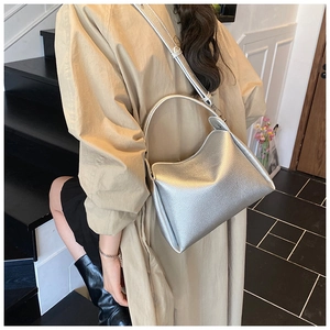 Sac seau argenté en cuir grainé porté par un mannequin dans un escalier moderne