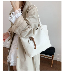 Detail of soft off-white tote bag with brown tassel charm on minimalist shoulder strap