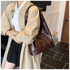 Detail of a dark brown large shoulder bag with shiny crinkled texture and bow decoration