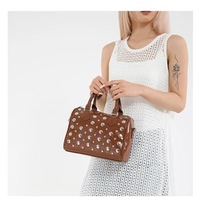 Brown patent leather Boston bag with silver rivets shown on a model with white background