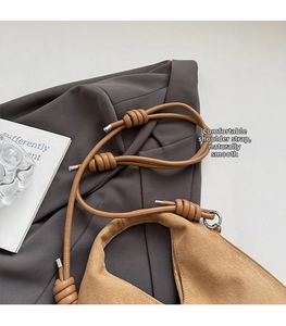 Close-up of minimalist brown suede bag featuring unique knotted strap with silver hardware