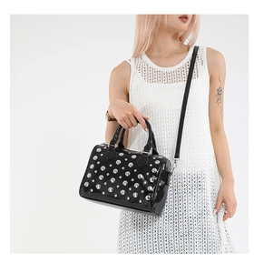 Detail of black glossy pillow bag featuring silver studs and detachable crossbody strap