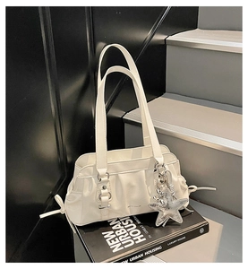 Close-up of a white pleated shoulder bag featuring a silver star pendant and side laces