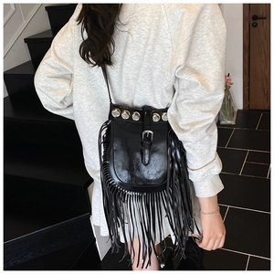 Detail of black tassel crossbody bag with metallic studs and fringe on indoor stairs