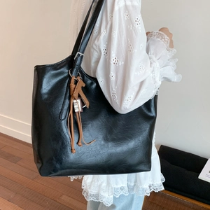 Detalle de un bolso tote negro de cuero con colgante de caballo, capacidad y textura