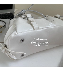 Detail view of silver anti-wear rivets on the bottom of a white glossy pleated handbag
