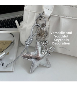 Detail showing a silver star charm with a metallic balloon dog pendant on a white tote bag