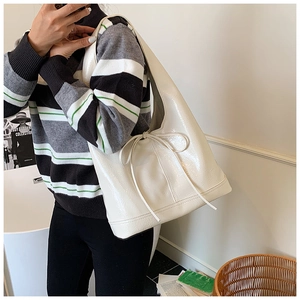Close-up of cream white glossy leather tote bag with elegant bow detail on a shoulder strap