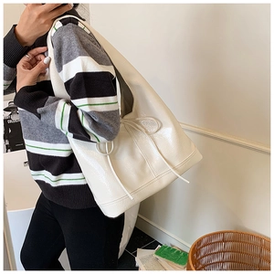 Detail of cream glossy leather tote bag with side drawstring showing premium texture