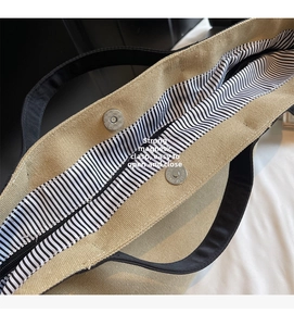 Detail view of large canvas tote bag featuring strong magnetic buckle and striped lining