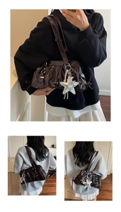 Detail of a dark brown patent leather underarm bag featuring a silver star pendant and buckles