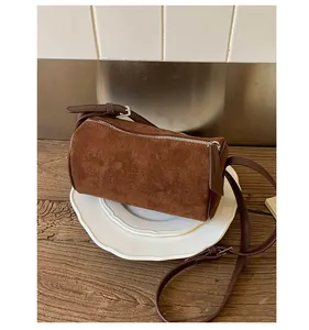 Detailed view of a brown suede cylinder bag with fine leather straps on a white ceramic plate