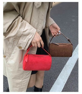 Detail of red and dark brown matte suede cylinder bags held against asphalt background