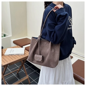 Brown suede tote bag shown on shoulder with hanging mini pouch detail and long strap