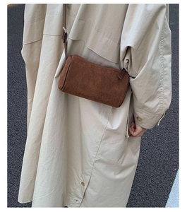 Close-up of a brown suede cylinder crossbody bag styled with a beige trench coat