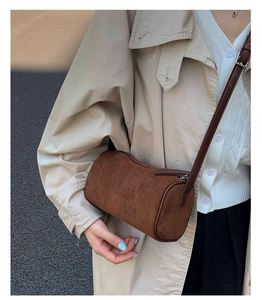 Detail of a dark brown cylindrical crossbody bag in matte suede texture for women