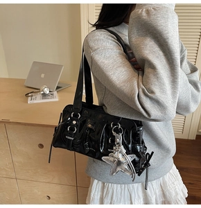 Detail of glossy black shoulder bag featuring silver star charm and buckle straps