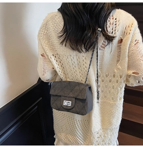 Detail of dark gray quilted chain bag worn over white knit sweater by a model