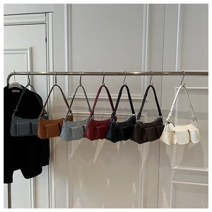 Multiple colors of minimalist leather underarm bags displayed on metal hooks