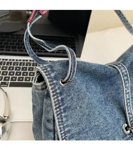 Détail du sac cabas en jean bleu montrant les anses cylindriques et les coutures contrastées