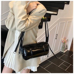 Detailed view of the glossy black cylindrical bag featuring shiny patent leather texture