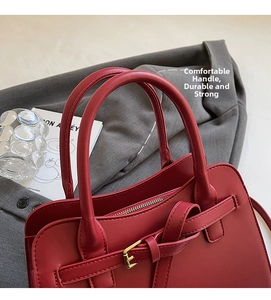 Detail shot of a red leather handbag with dual handles and decorative metal buckles