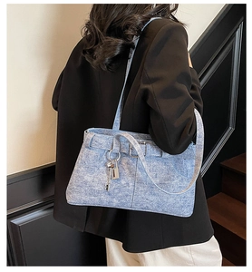 Detail of light blue denim tote bag with metal buckles and silver key pendant accessory