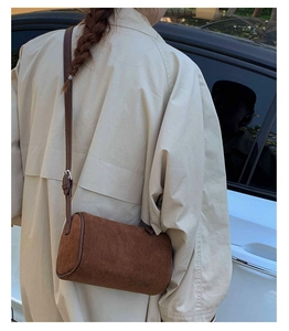 Close-up of brown suede barrel bag worn over a beige trench coat in a street setting
