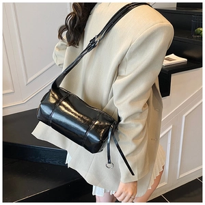 Detail view of glossy black cylindrical shoulder bag in a stylish minimalist interior