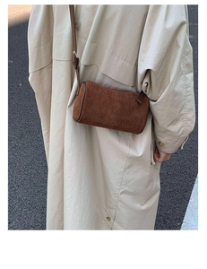 Detail of a brown suede cylinder crossbody bag shown on a model wearing a beige trench coat