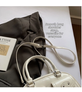 White glossy leather handbag detail with detachable shoulder strap and rivet accents