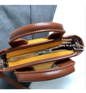 Close-up of smooth metal zipper and brown leather trim on a yellow canvas pillow bag
