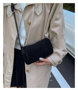 Street style view of a black frosted leather cylindrical bag paired with a beige coat