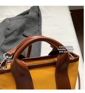 Detail view of yellow canvas handbag with brown leather handles and sturdy metal hardware