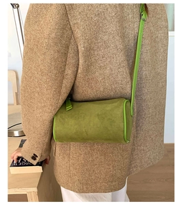 Detail view of green suede cylinder bag with leather piping and silver buckle on a strap