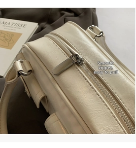 Detail view of the silver metal zipper and wrinkled texture on the cream shoulder bag