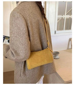 Detail of a bright yellow cylindrical crossbody bag in matte suede texture worn by model