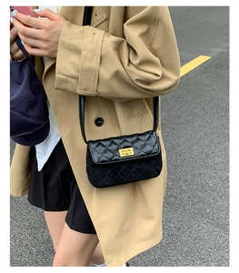 Detail of black quilted crossbody bag with golden metal clasp on a khaki trench coat