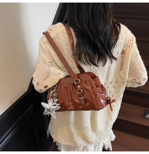 Detail of a shiny dark brown hobo bag featuring a metallic silver star charm and pleats