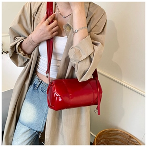 Red patent leather cylinder shoulder bag shown on model with shiny mirror finish