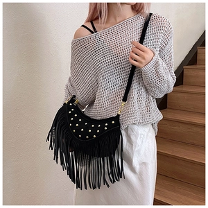 Detail of black fringe crossbody bag with gold rivets and bohemian tassel style