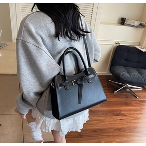 Rear view of model holding a black structured handbag with decorative belt and shoulder strap