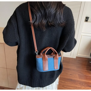 Detail of blue denim canvas tote bag with brown leather trim worn by model
