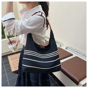 Detail of navy nylon tote with white stripes and brown leather handle on a shoulder