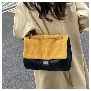 Detail of yellow quilted suede flap and silver chain strap on a black leather tote